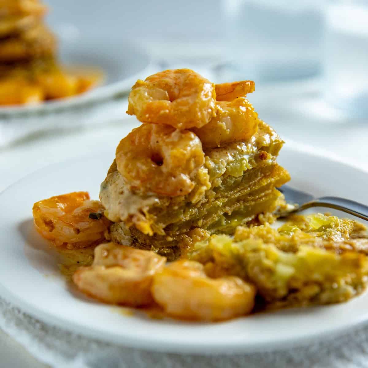 Fried green tomatoes stacked on white plate with shrimp creole sauce poured on top.