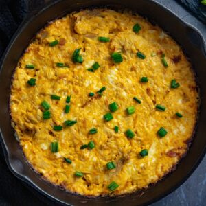 Baked dip topped with sliced green onions in a skillet.
