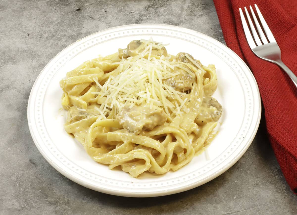 tetrazzini topped with parmesan cheese in white round plate with red napkin and fork on the side