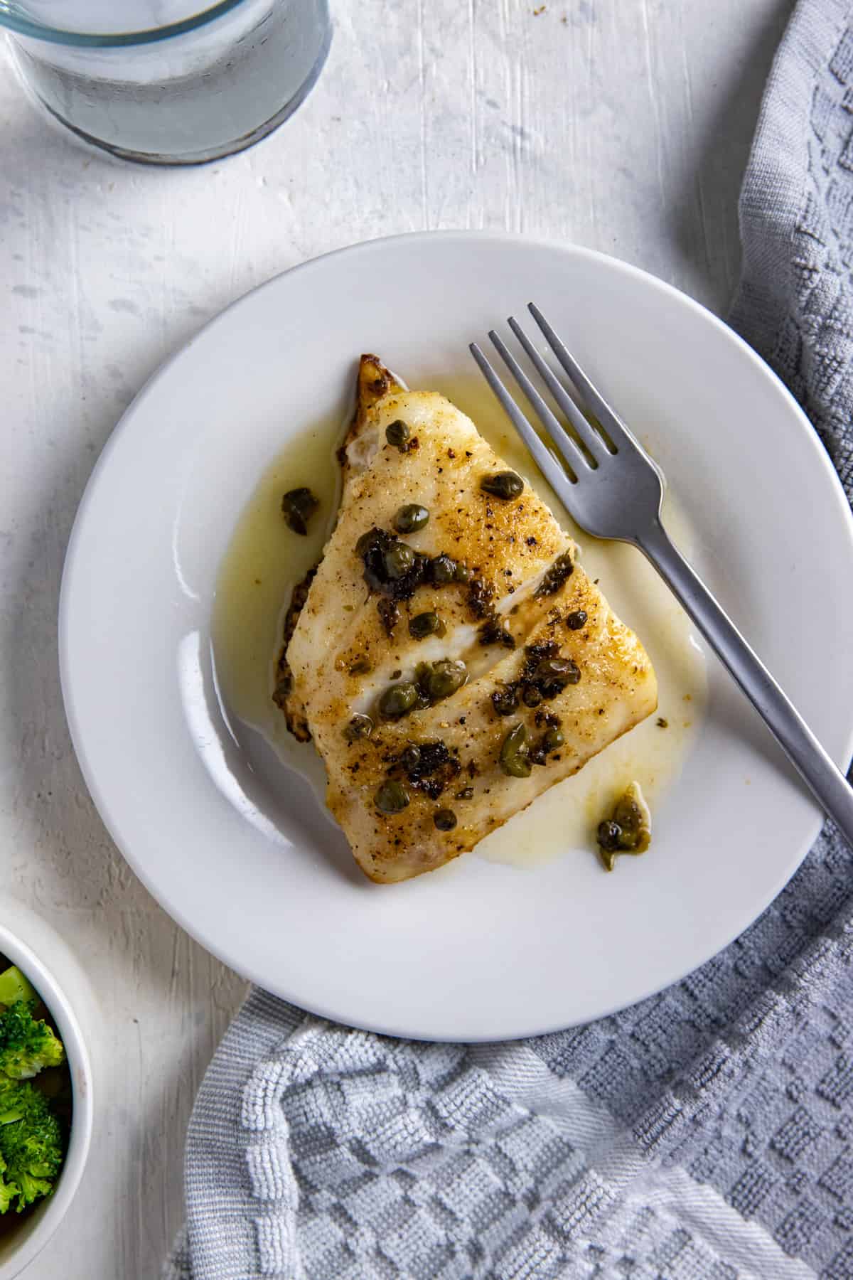 baked snapper topped with capers on white plate with fork