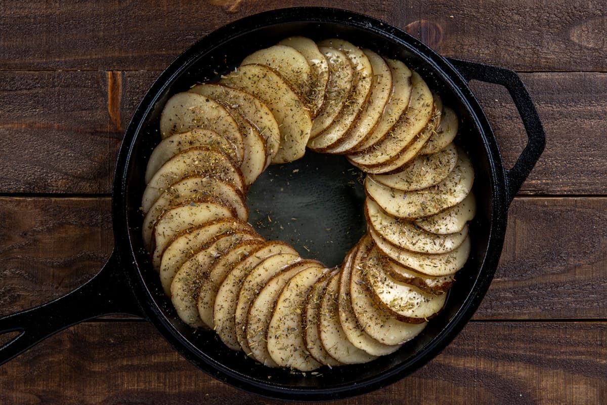 sliced potato in skillet with butter and seasonings on top