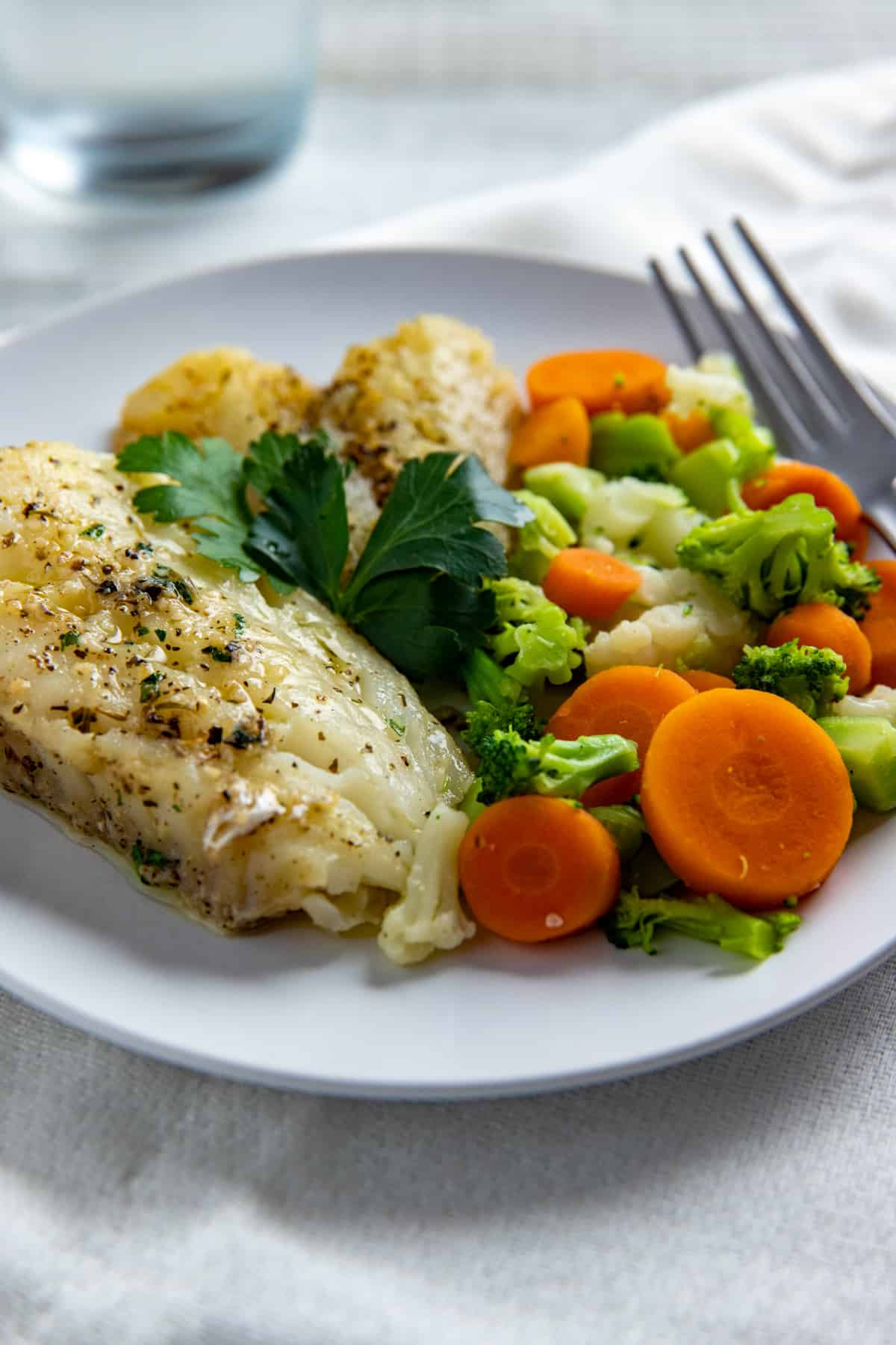 cooked cod on white plate with broccoli, cauliflower, and carrot mixture