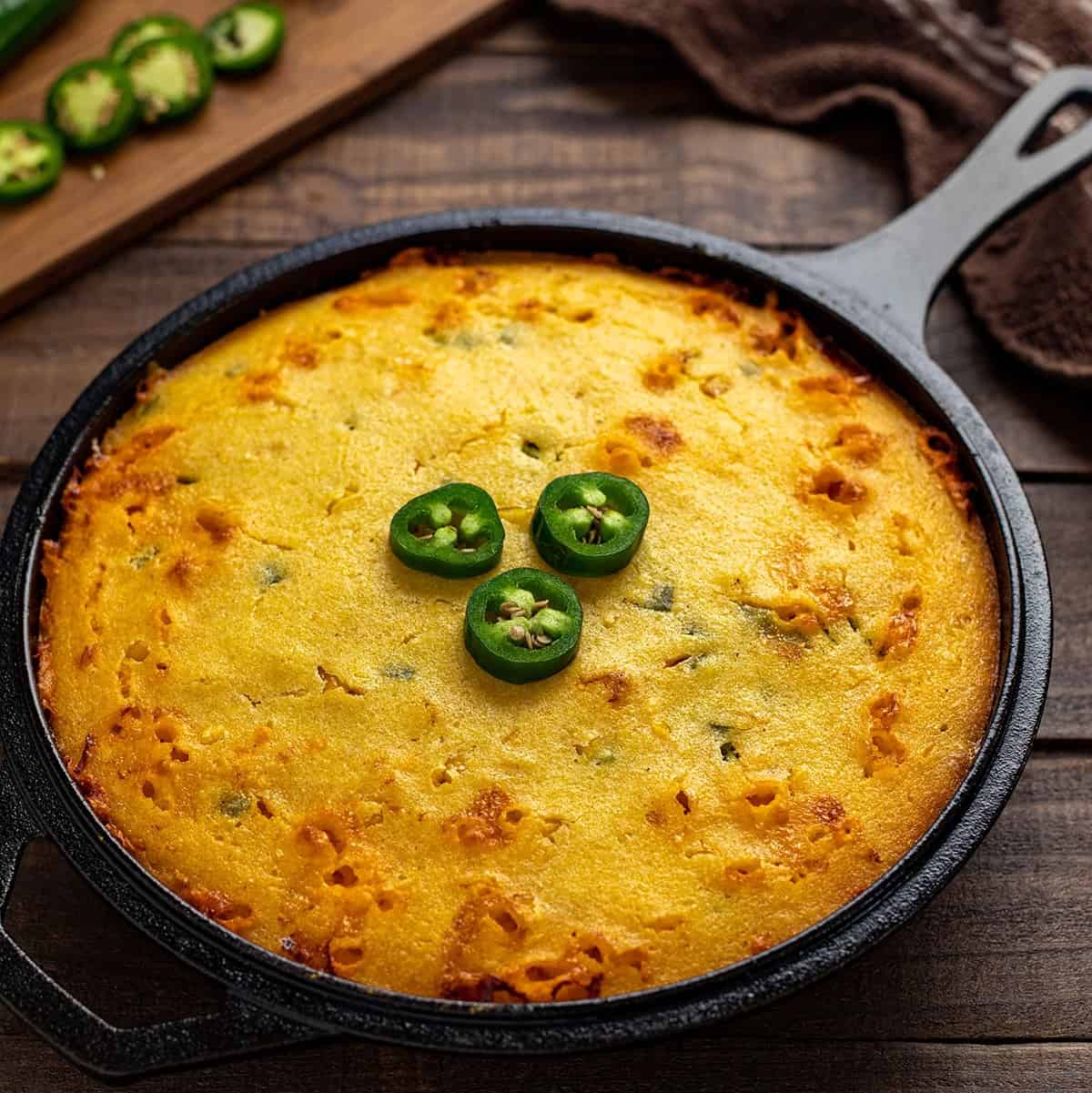 baked jalapeno cornbread in cast iron skillet with 3 jalapeno slices on top
