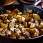 crispy fried sliced potatoes and bits of onion and garlic in a cast iron skillet