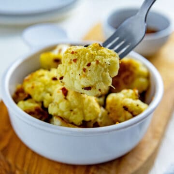 Bowl of parmesan roasted cauliflower with a fork holding a cauliflower floret.