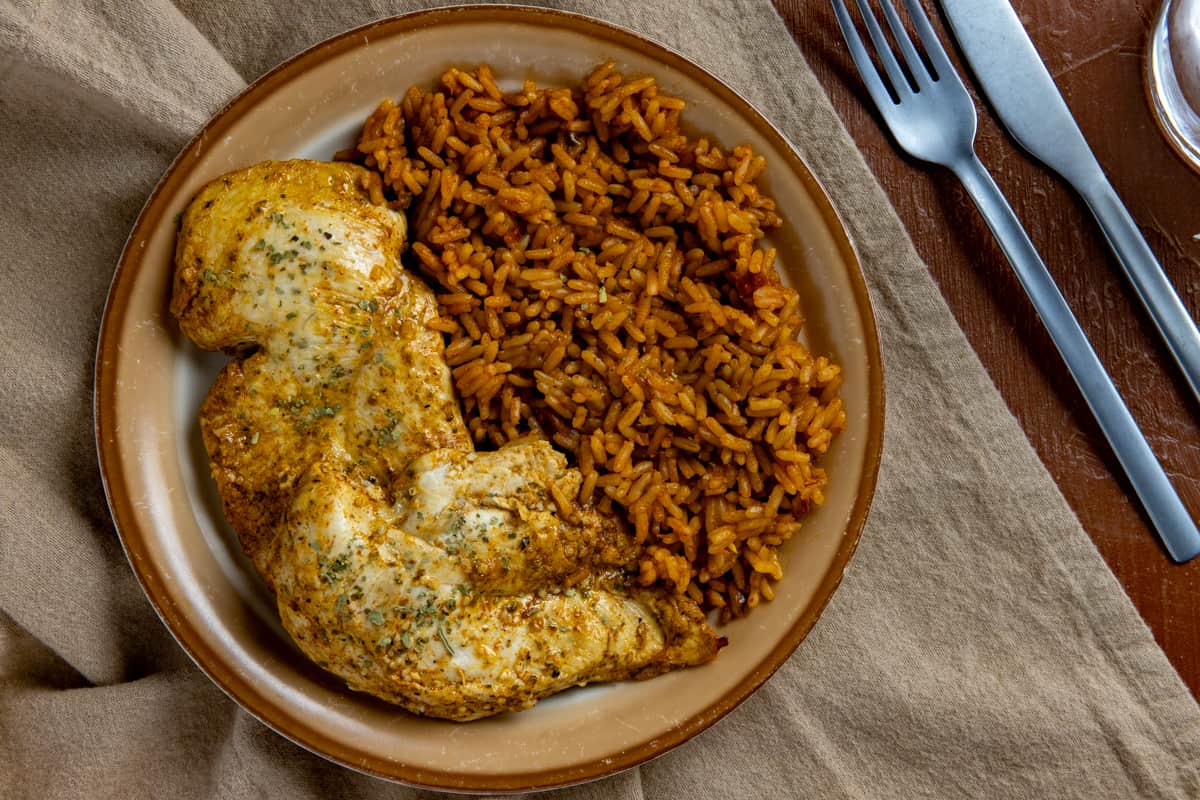Baked chicken breast on brown plate with a side of Mexican rice.