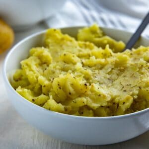 Mashed potatoes in white bowl with silver spoon inserted.