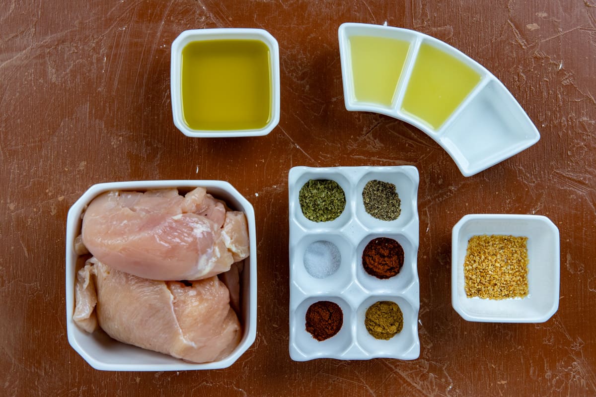 Ingredients measured out in white individual containers on brown wooden countertop.