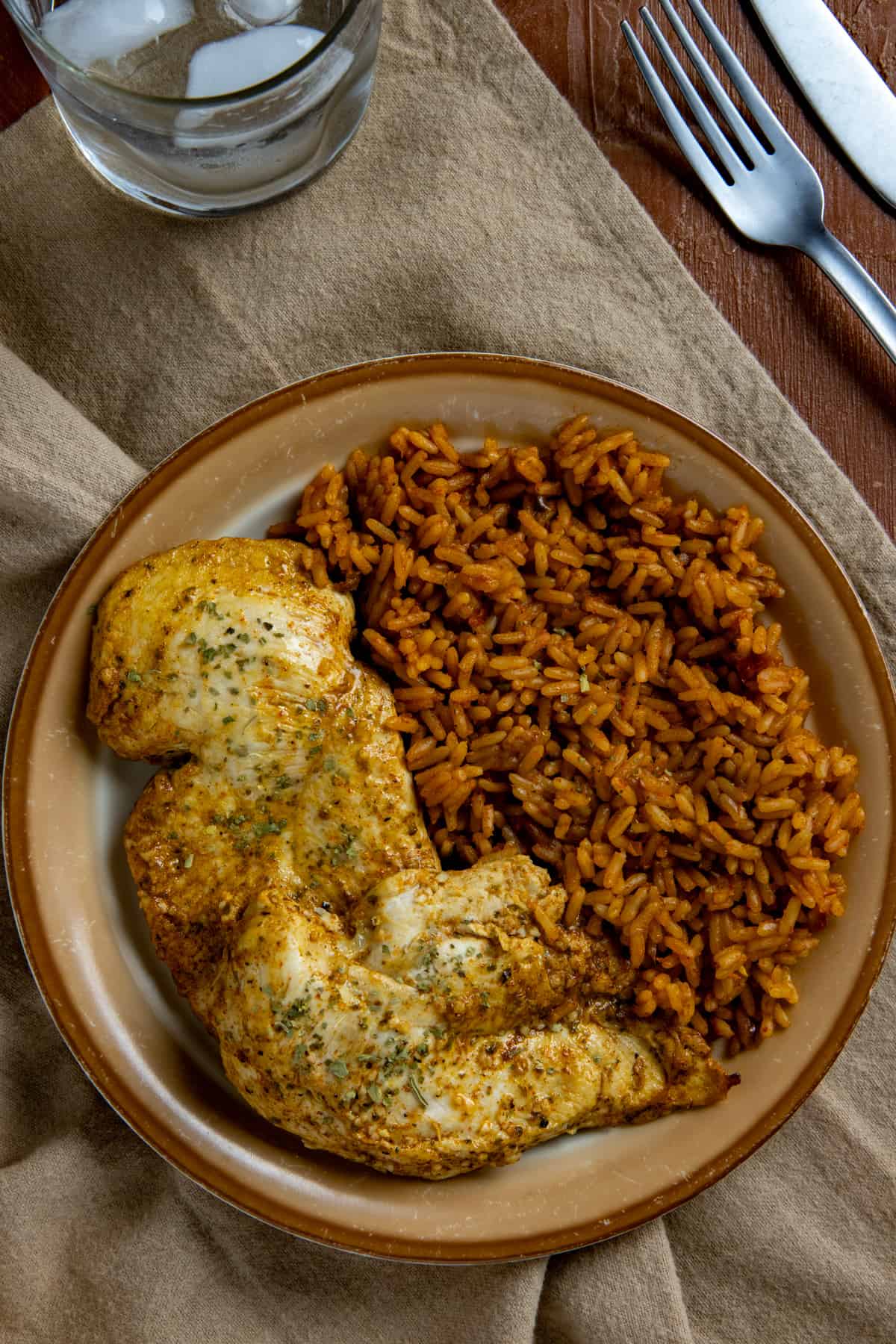 Baked chicken breast on brown plate with a side of Mexican rice.