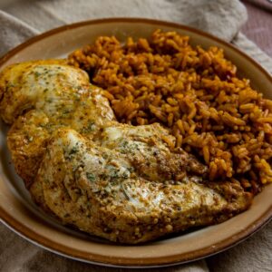 Baked chicken breast on brown plate with a side of Mexican rice.