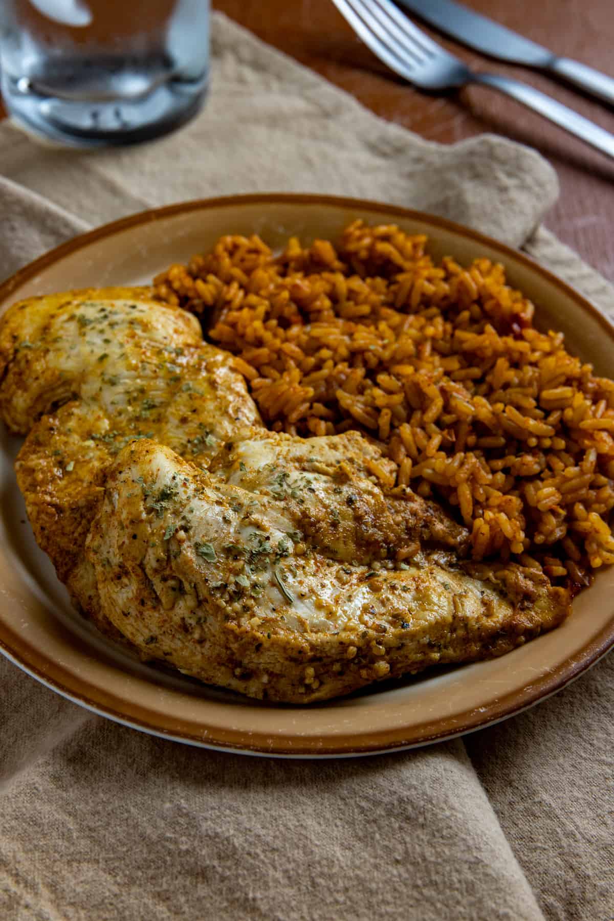 Baked chicken breast on brown plate with a side of Spanish rice.