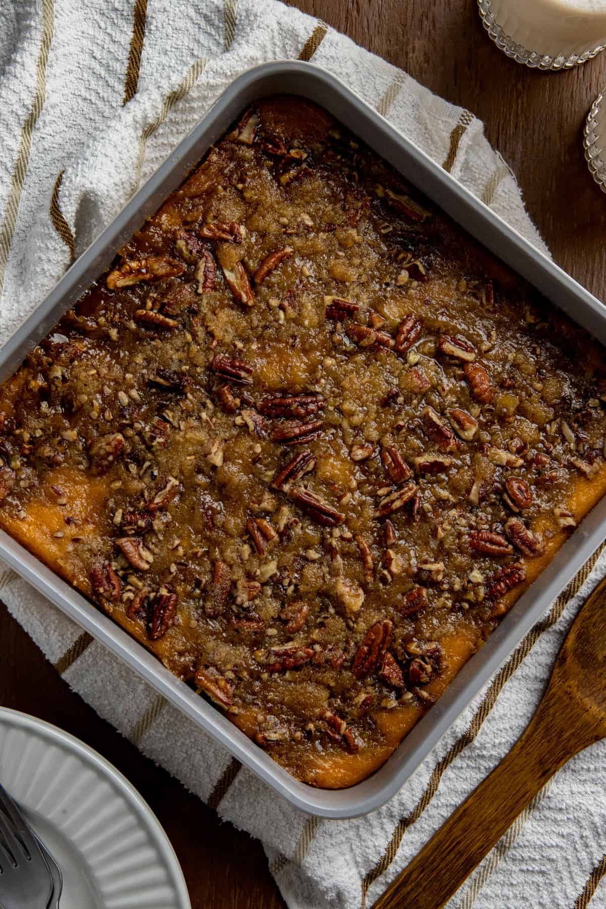 Baked sweet potato casserole in square aluminum pan. Wooden spoon on white napkin next to casserole dish.