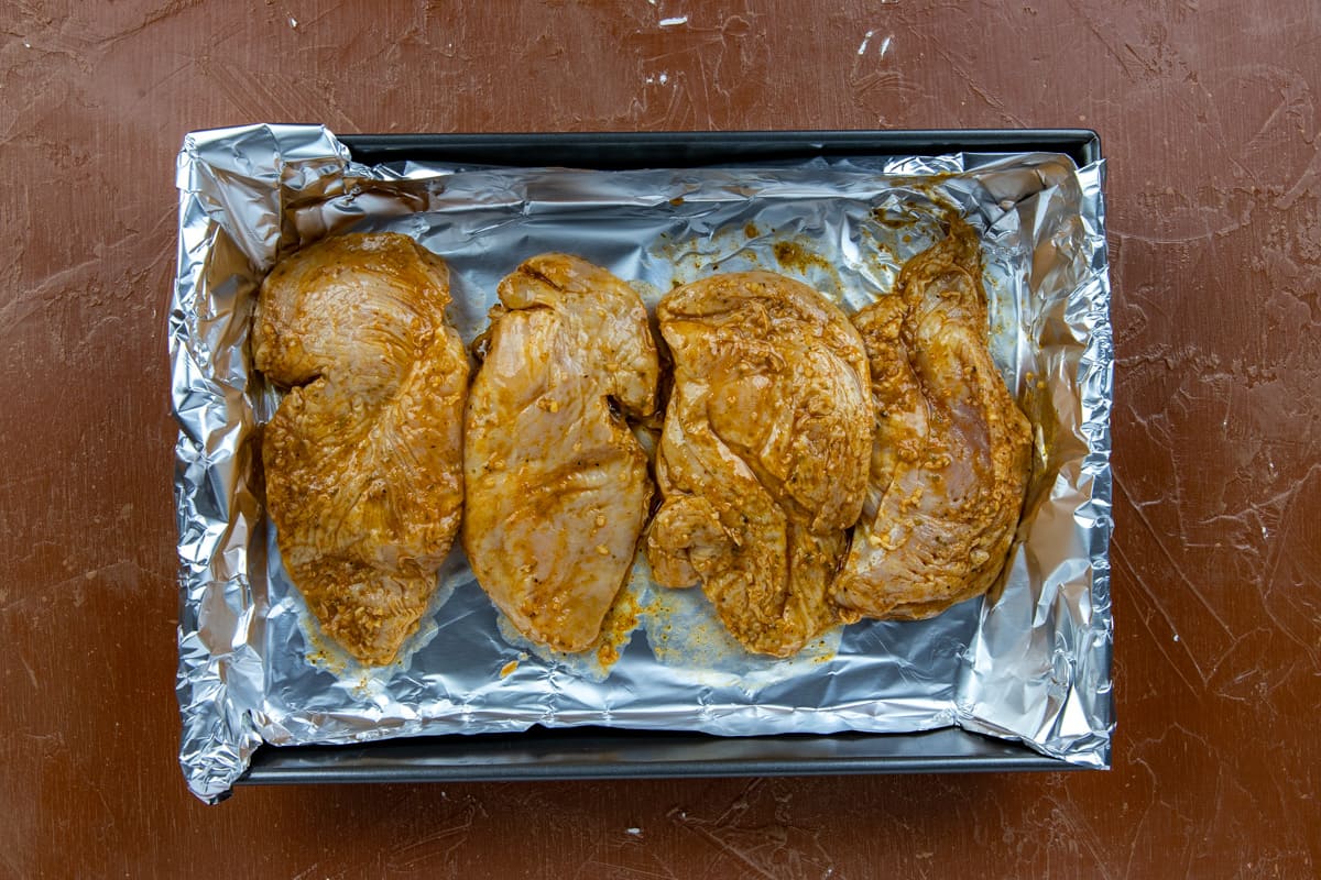 Raw chicken breasts on sheet pan lined with foil.
