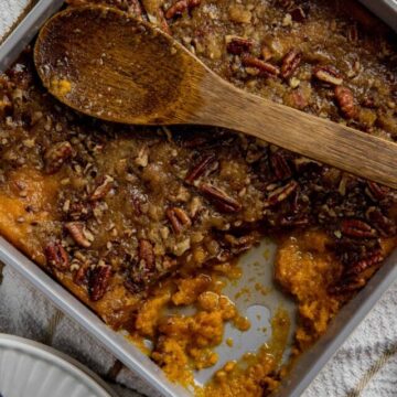 Baked casserole in square dish with wooden spoon on top and one serving removed.