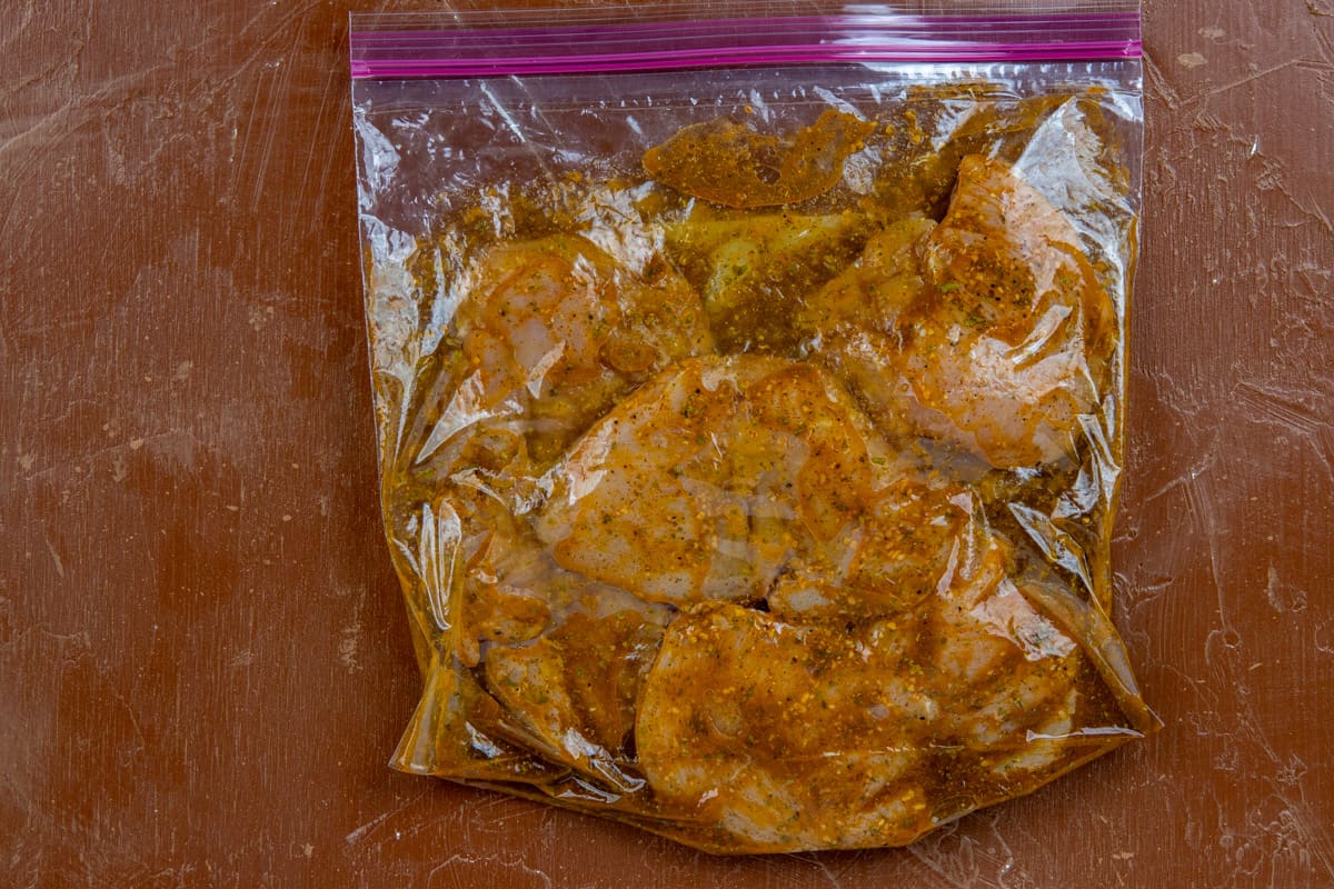 Raw chicken and seasonings in gallon ziplock bag.