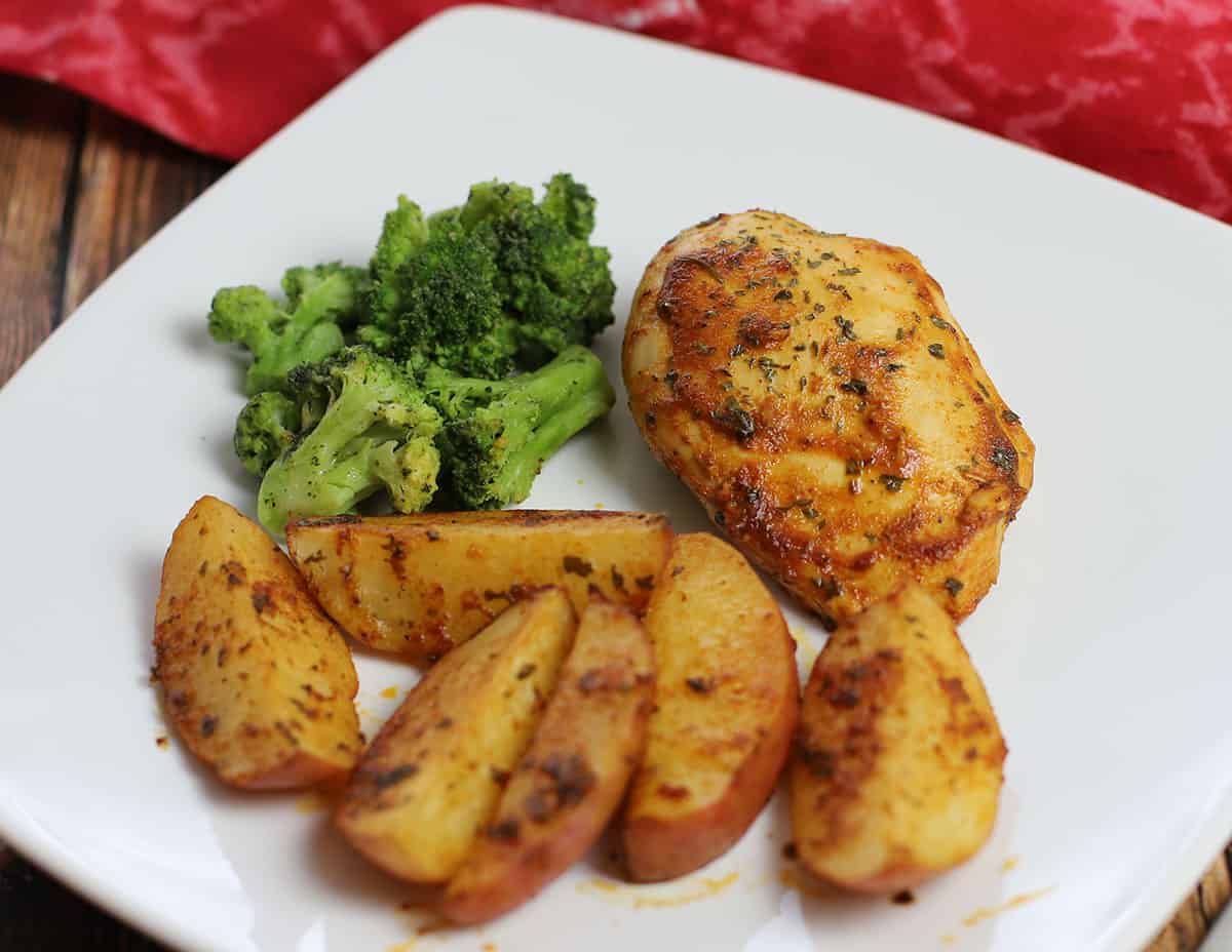 Baked chicken and potatoes on white plate with steamed broccoli on the side.