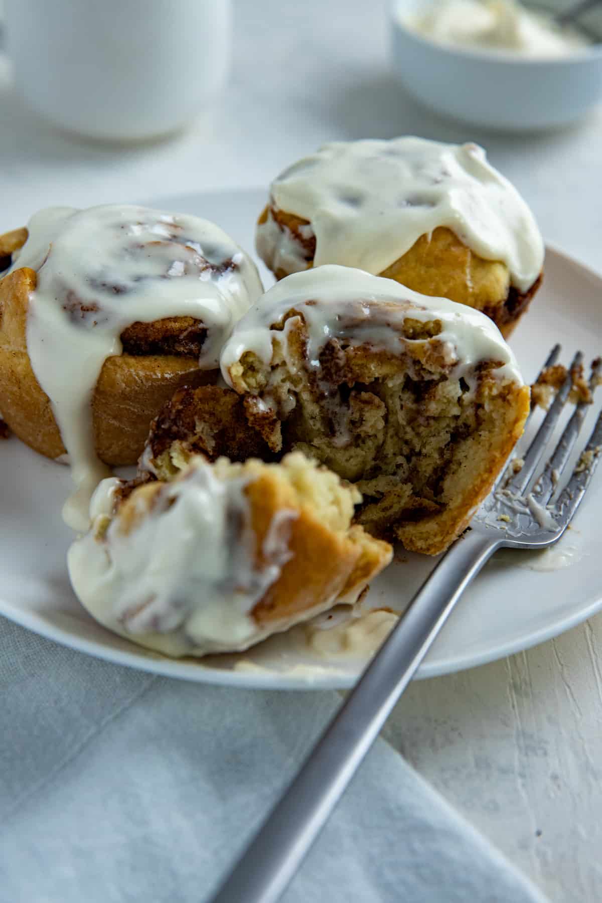 Three baked cinnamon rolls with cream cheese frosting on white plate with fork.