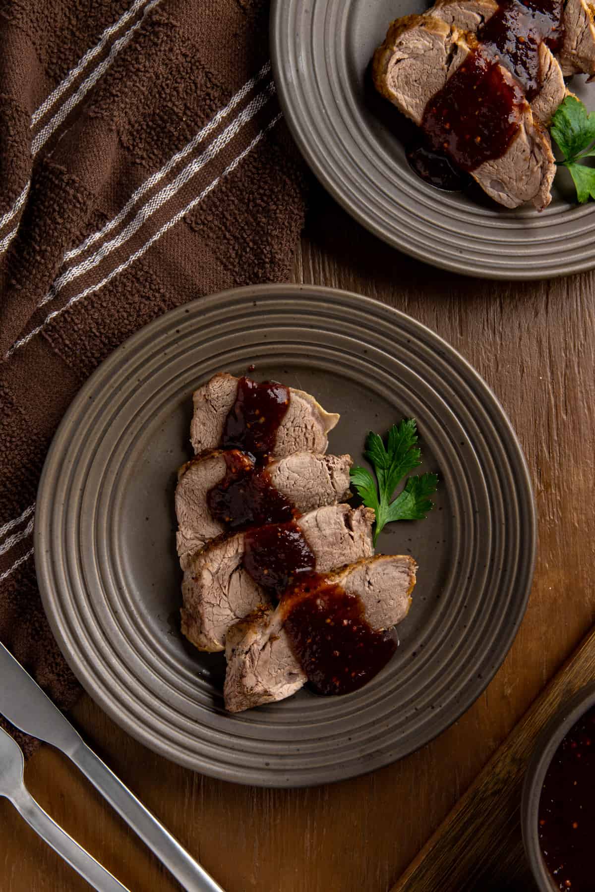 Four sliced of cooked pork tenderloin topped with sauce on brown plate.