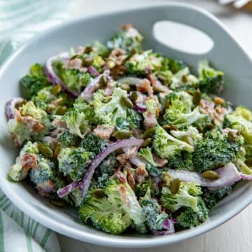 Tossed broccoli bacon salad in white bowl.