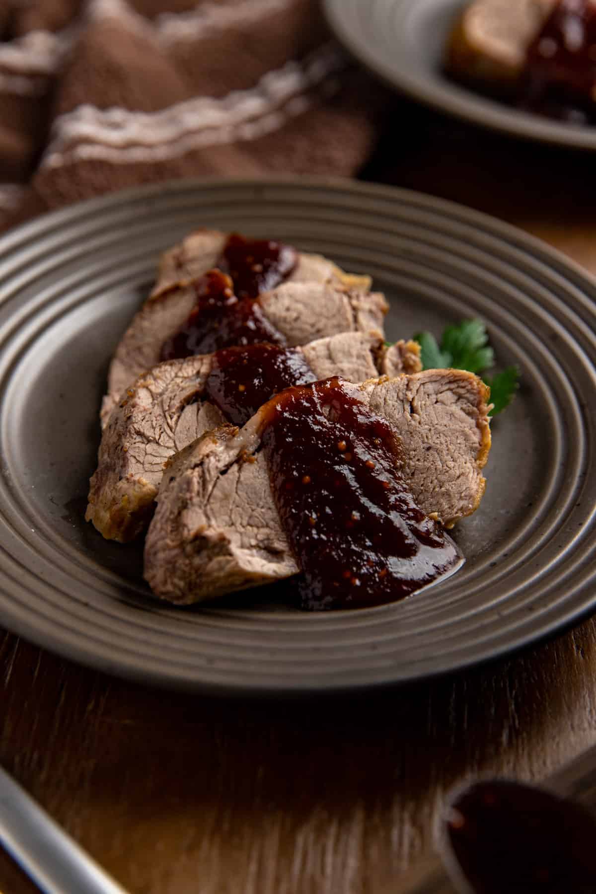 Four sliced of cooked pork tenderloin topped with sauce on brown plate.