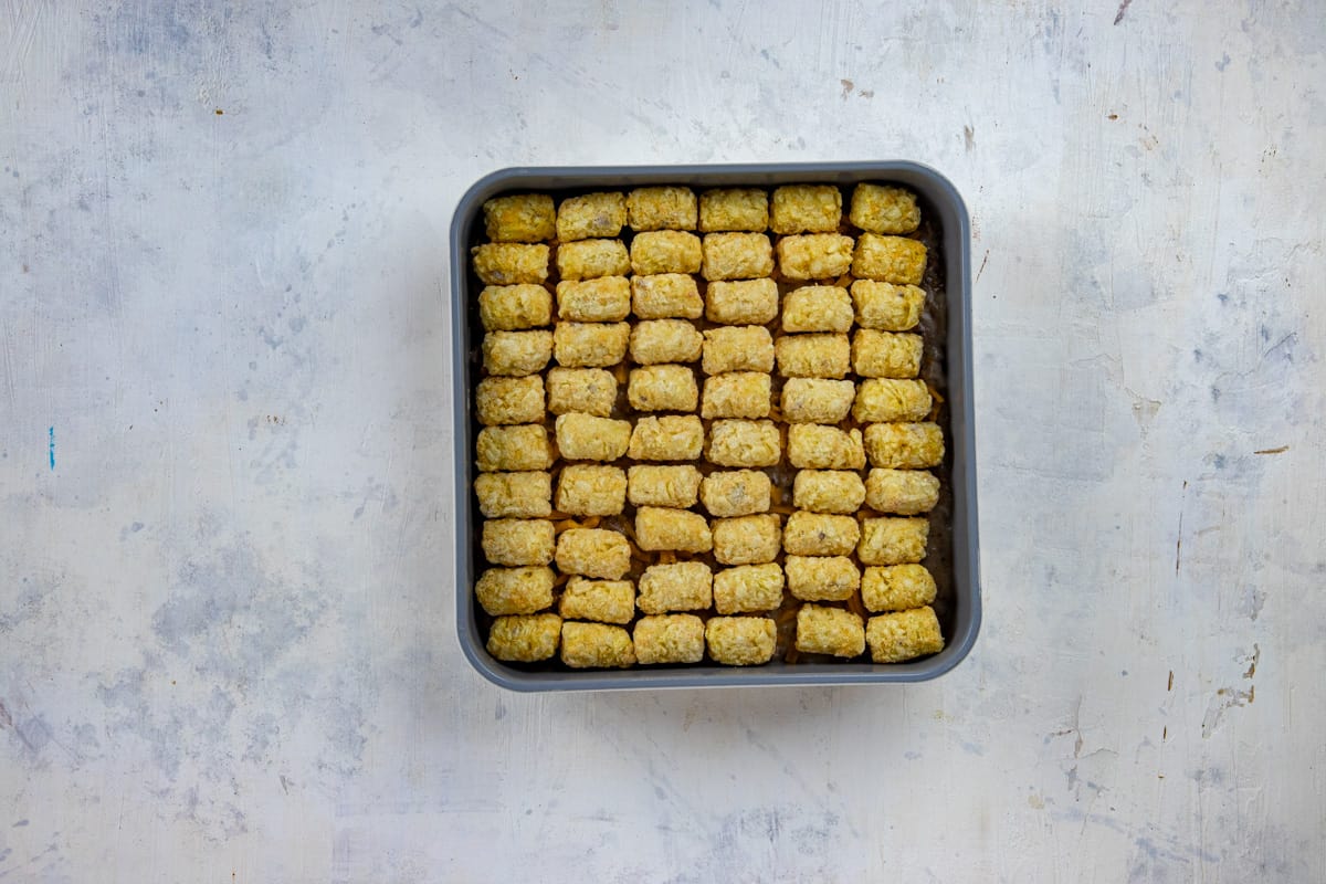A layer of tater tots spread on top of beef mixture in the same square pan.