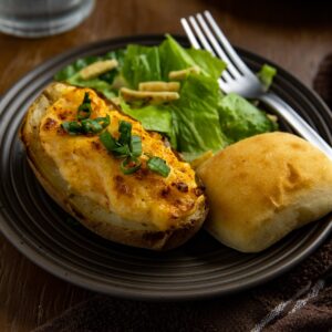 Two baked potato halves on brown plate with roll and side salad.