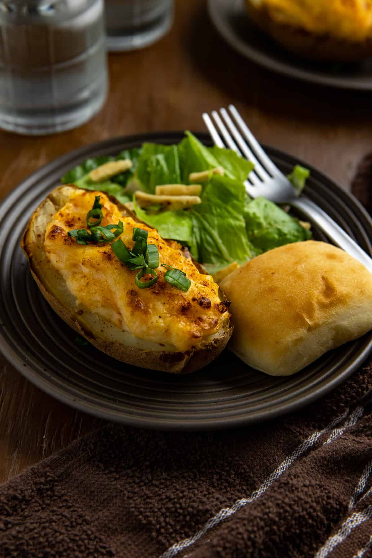 Two baked potato halves on brown plate with roll and side salad.