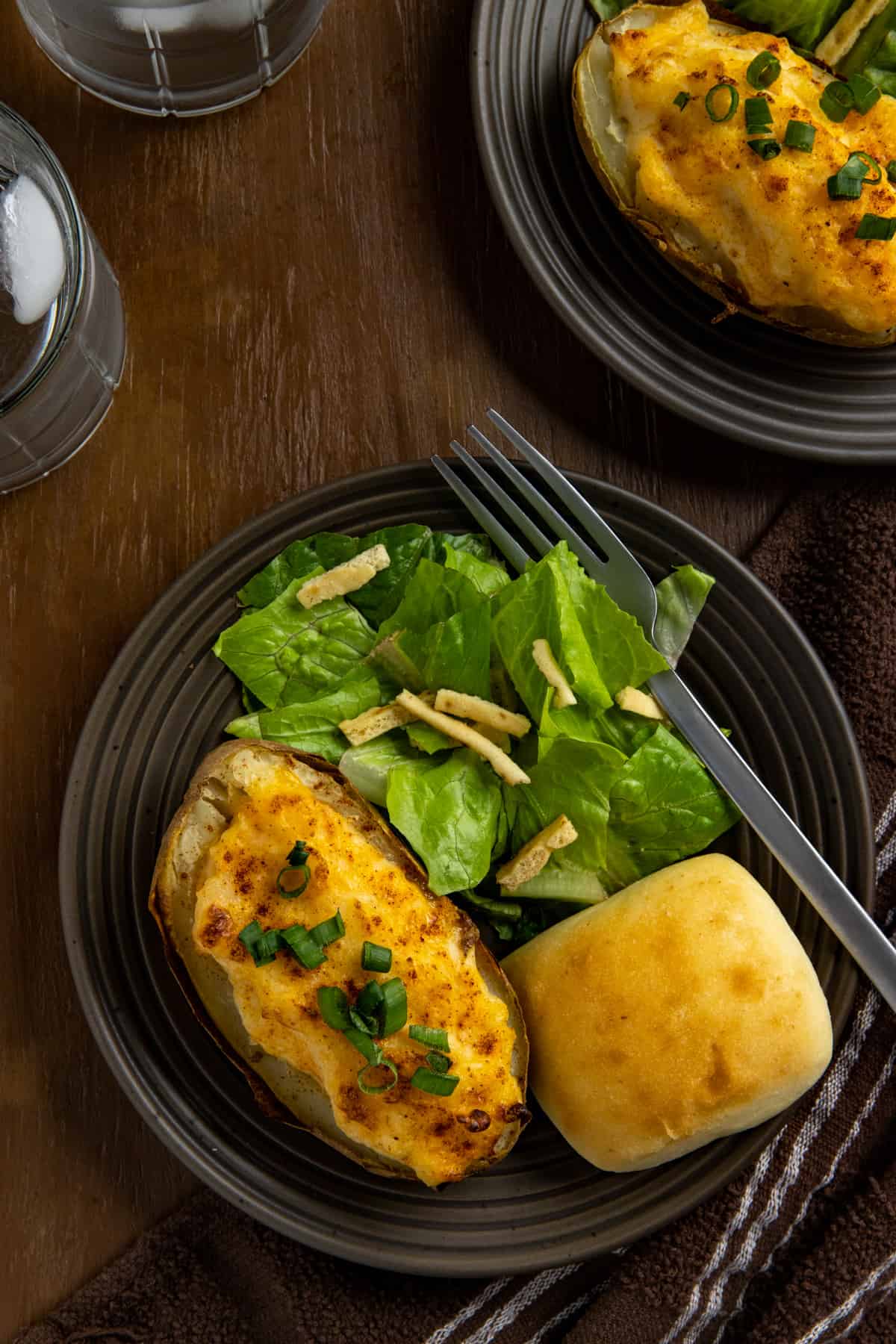 Two baked potato halves on brown plate with roll and side salad.