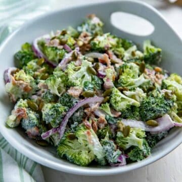 Tossed broccoli bacon salad in white bowl.