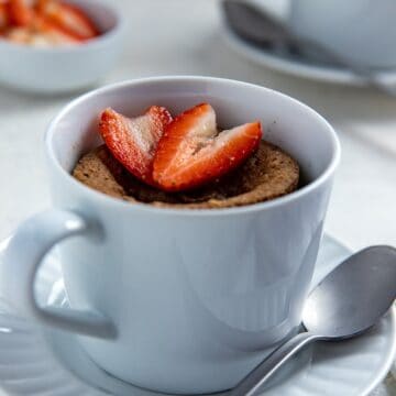 Cooked mug cake in white dish with sliced strawberry on top.