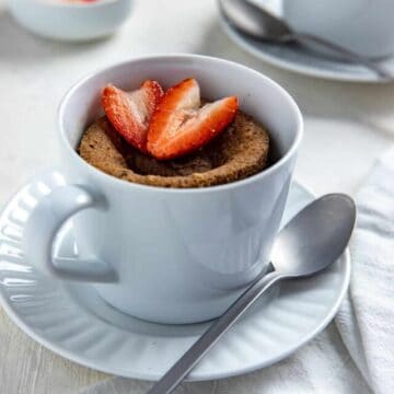 Cooked mug cake in white dish with sliced strawberry on top.