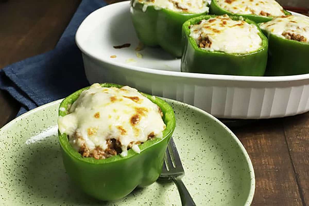 Cooked stuffed bell pepper on green plate with fork.  Additional baked bell peppers in background in a white baking dish.