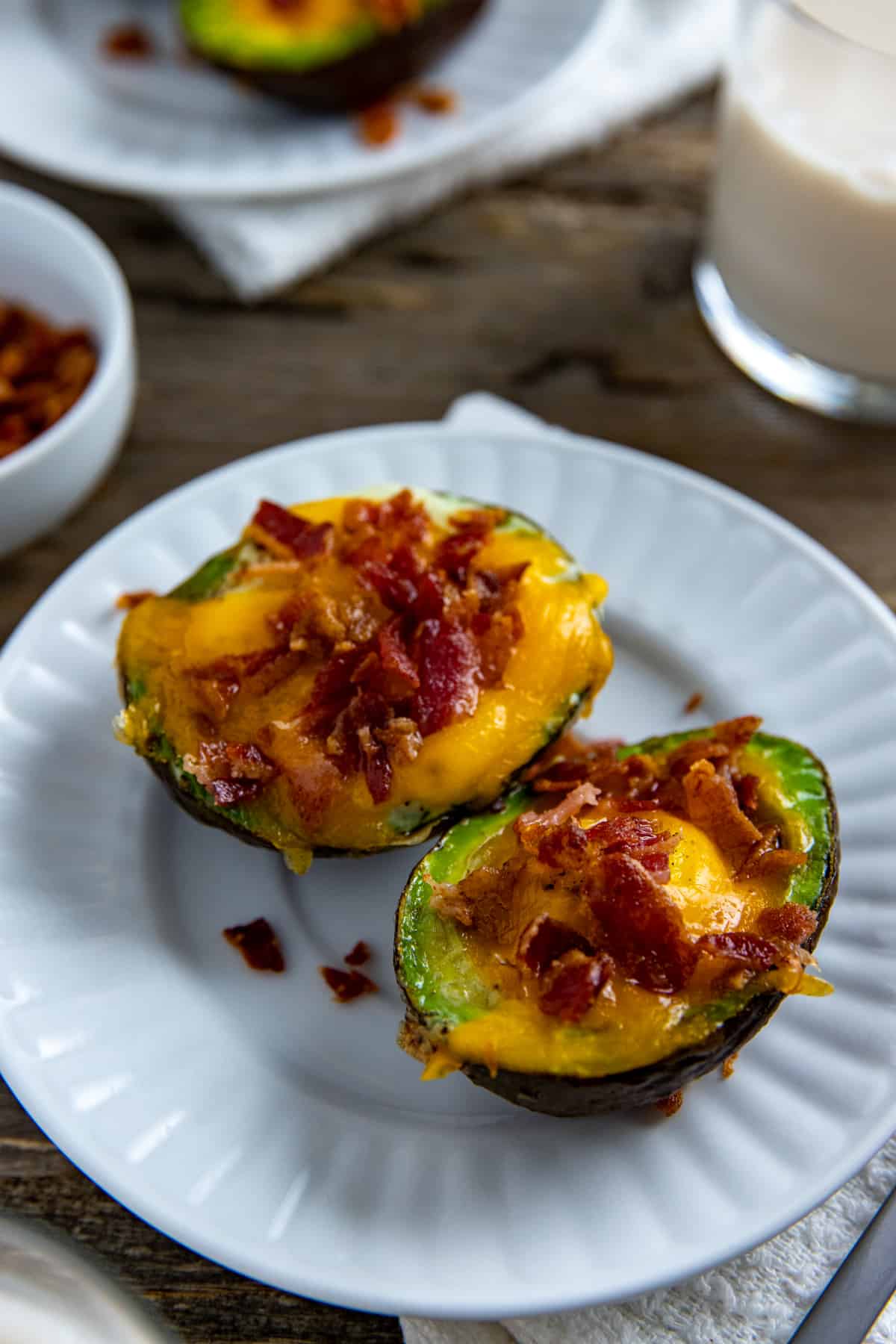 Two baked avocado egg boats on white plate.