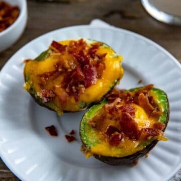 Two baked avocado egg boats on white plate.