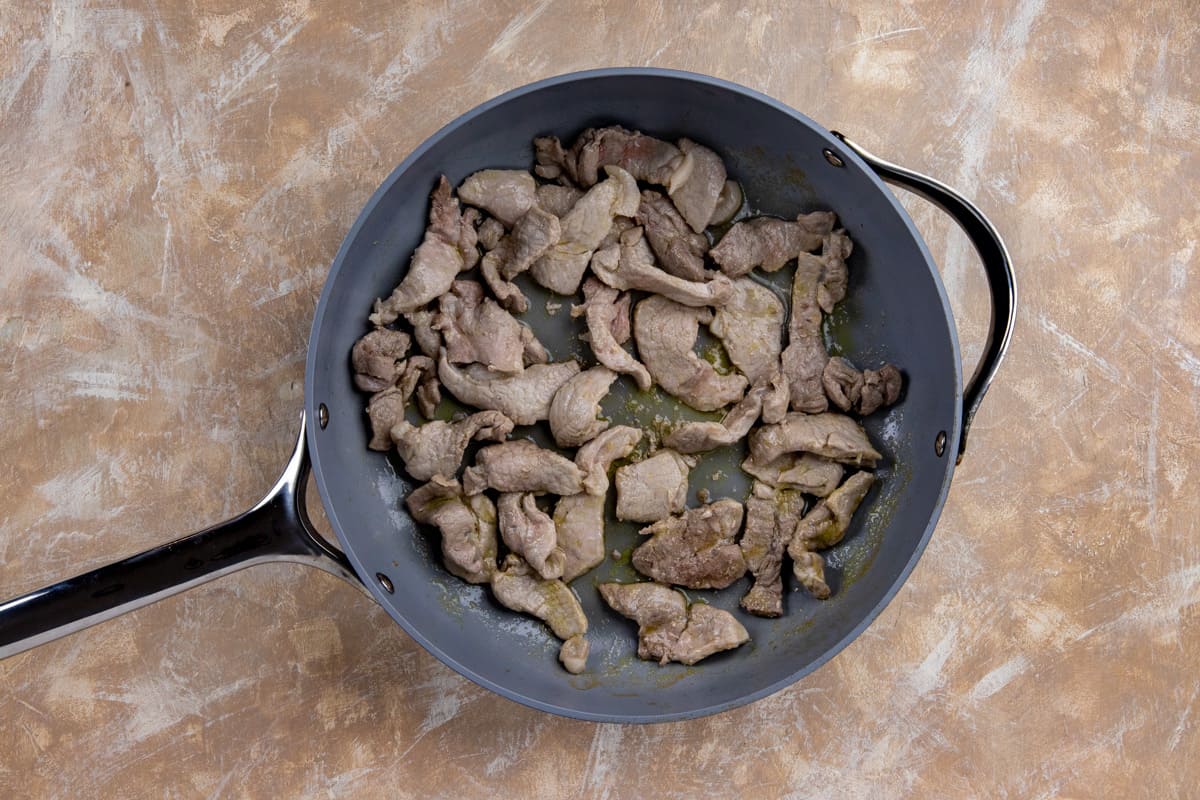 Sliced pork that has been sauteed in a large skillet.