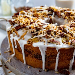 Whole cake with frosting and topping on round wooden cake platter.