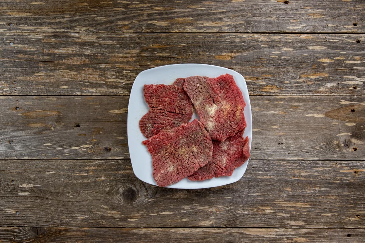 Raw seasoned minute steaks on square white plate.