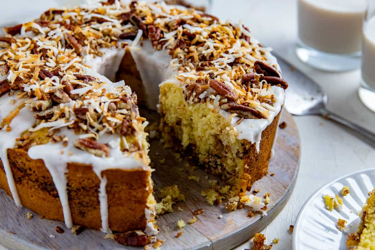 Toasted Coconut Coffee Cake on wooden cake platter with one slice removed.