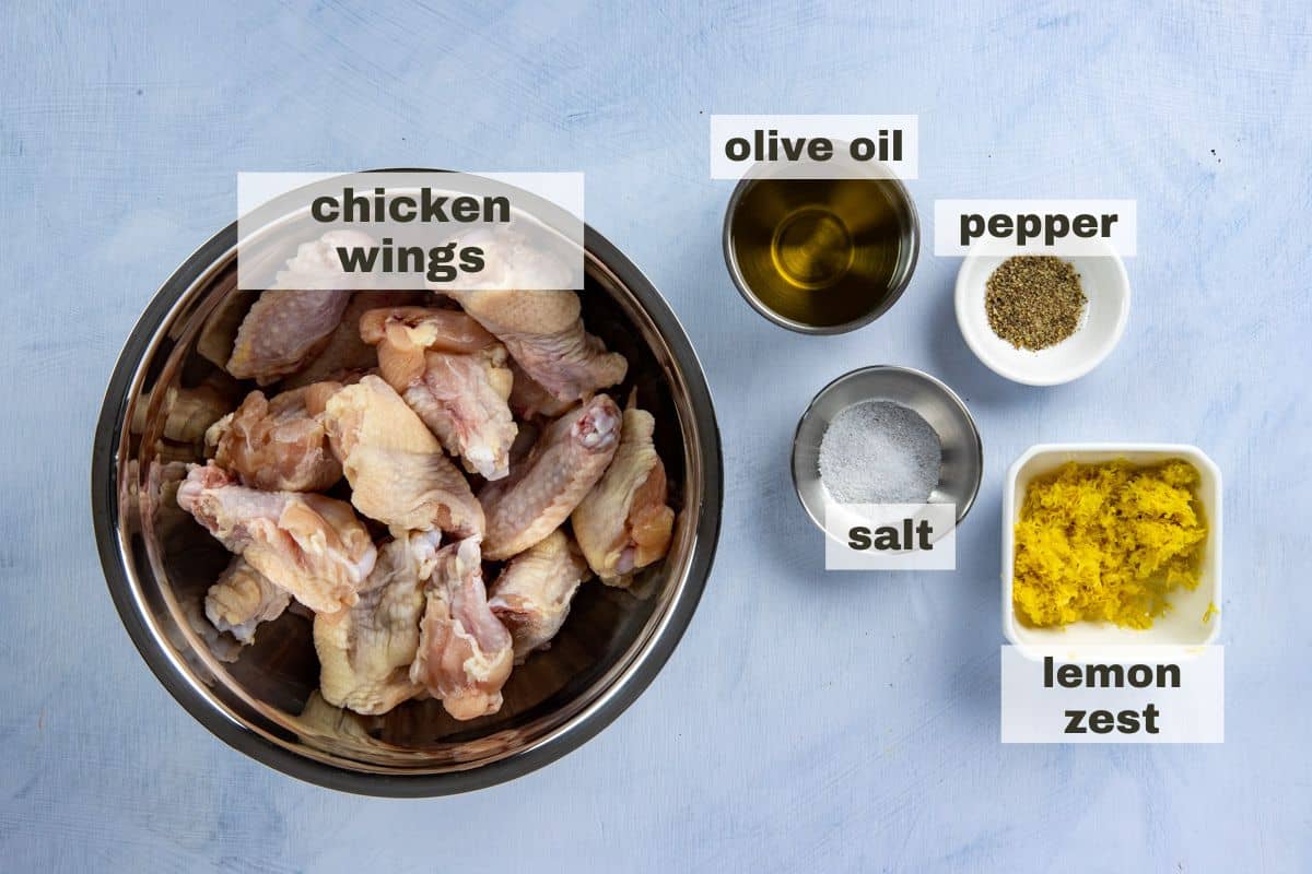 Recipe ingredients measured out in individual bowls. Raw chicken wings, olive oil, pepper, salt, and lemon zest.