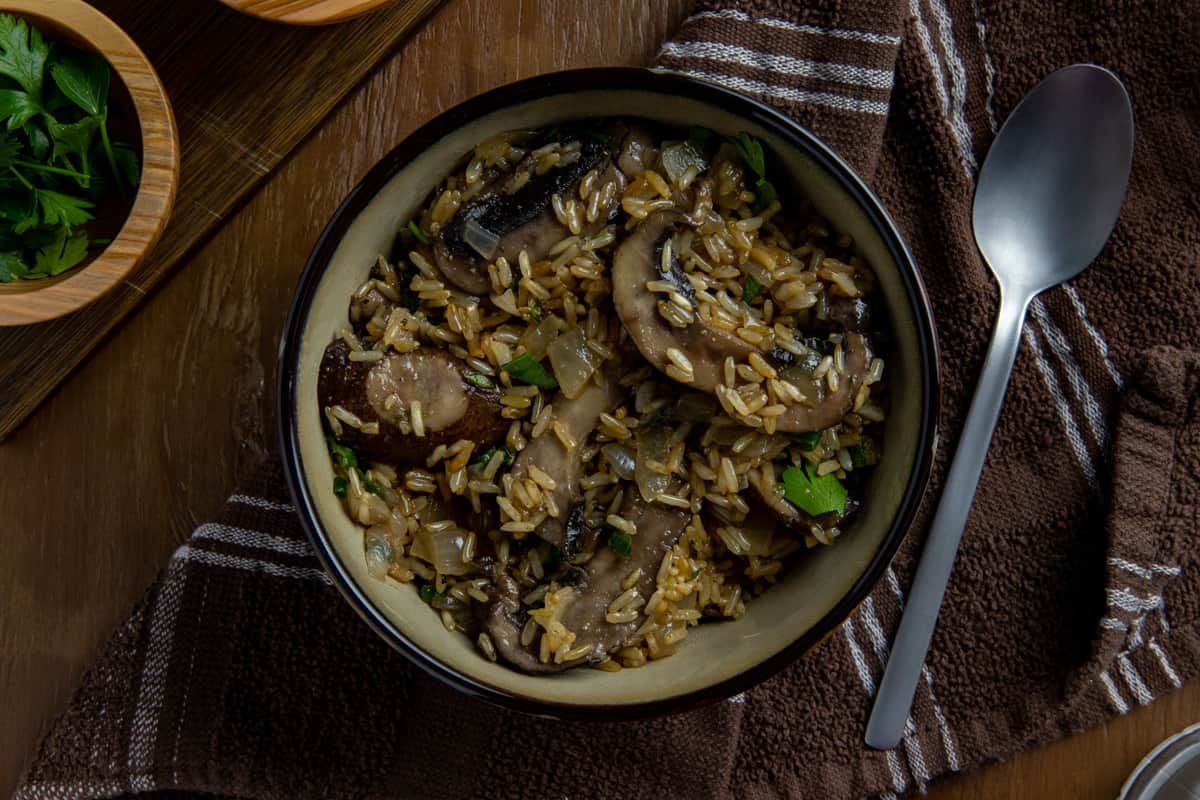 Cooked mushroom rice in brown bowl with spoon on the side.