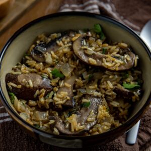 Cooked mushroom rice in brown bowl with spoon on the side.