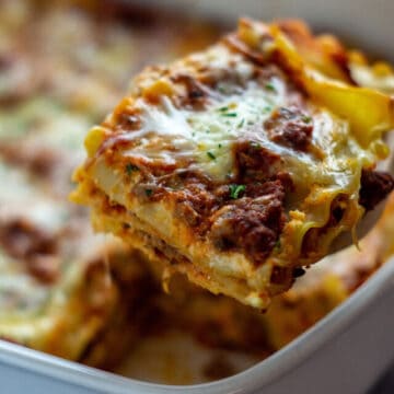 Baked lasagna in casserole dish with a serving being removed.