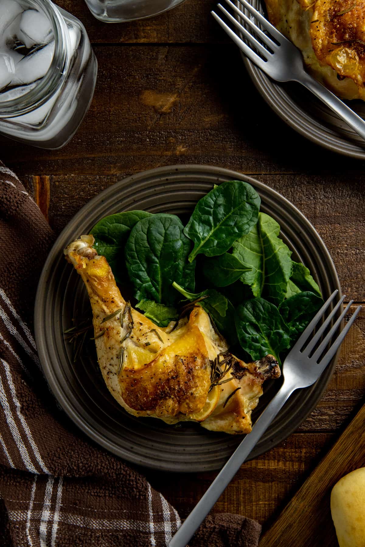 Overhead view of baked chicken leg quarter on brown plate with fresh baby spinach on the side.