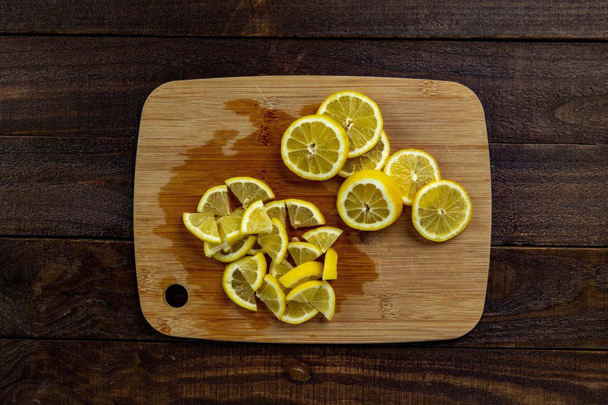 Wooden cutting board with sliced and quartered lemon slices.