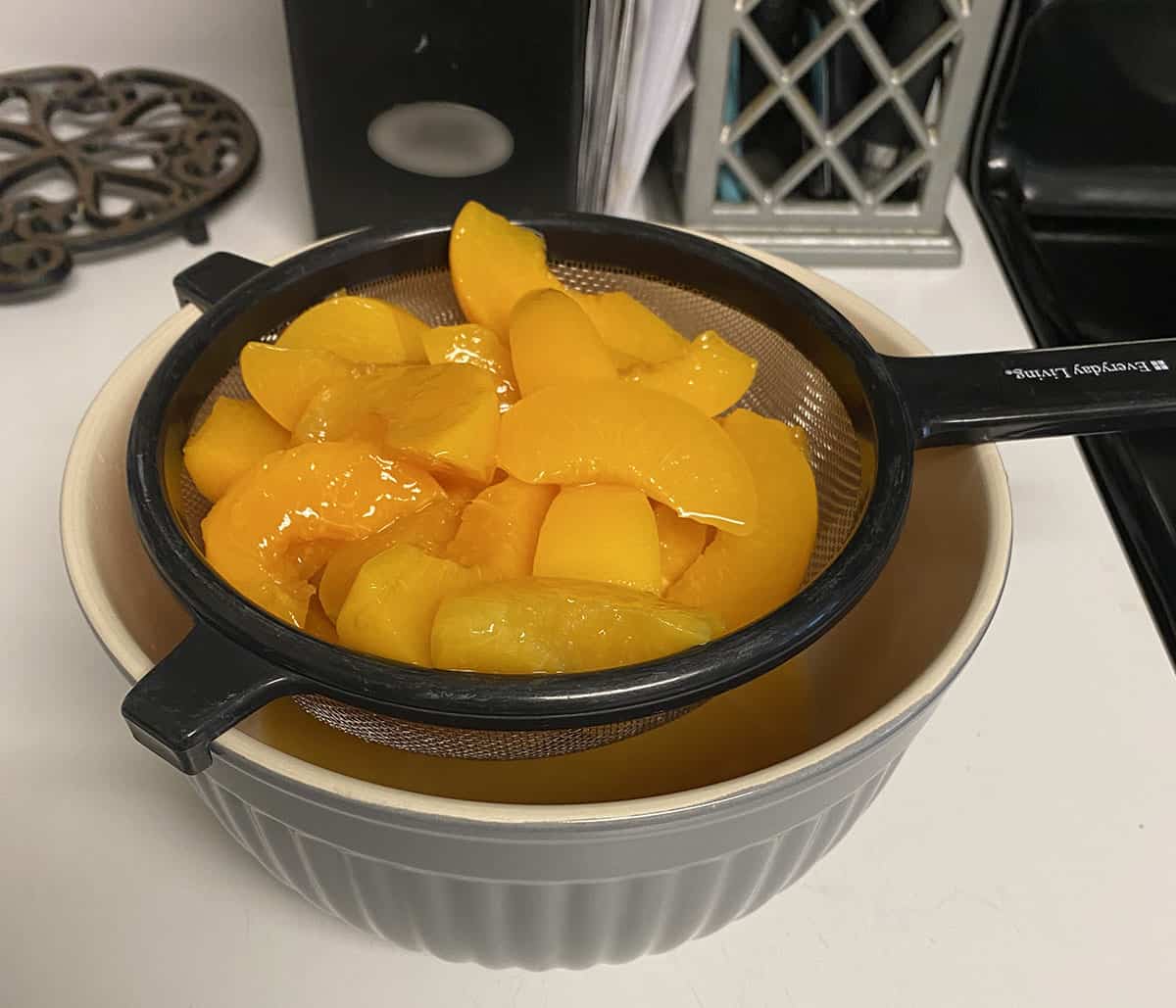 Canned sliced peaches in a strainer over a bowl collecting the peach juice.