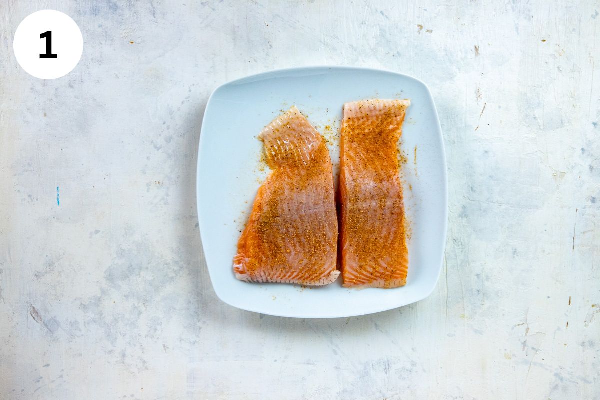 Two raw salmon fillets seasoned with Cajun seasonings on a white plate.