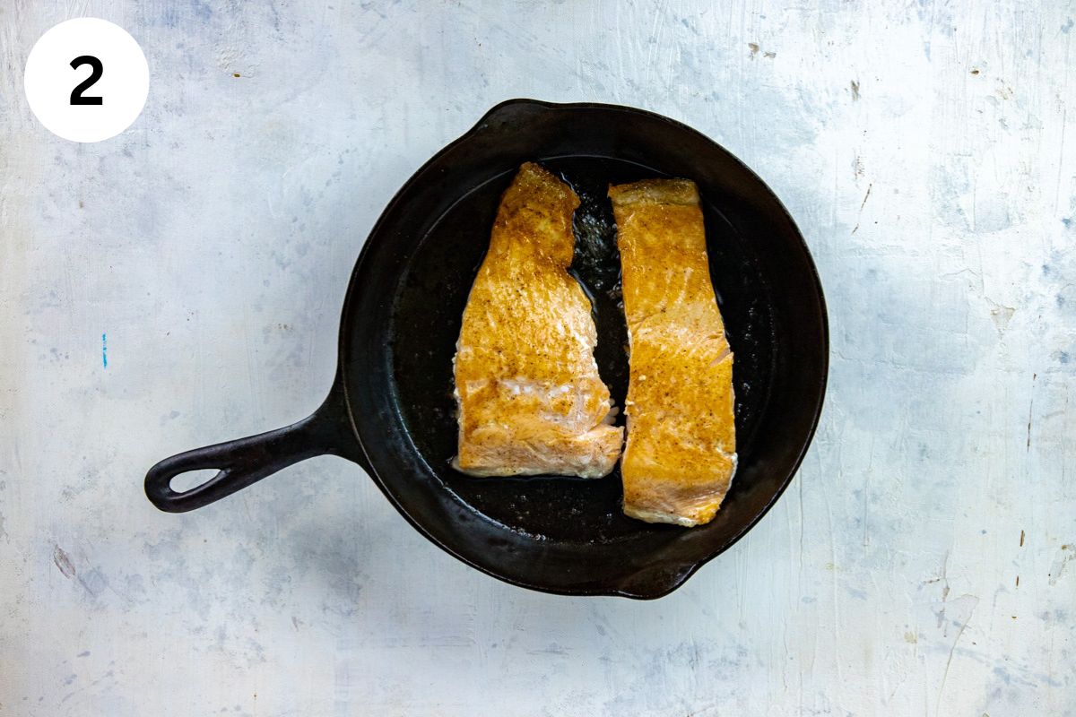 Two seared salmon fillets in a cast iron skillet.