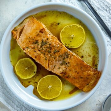 Baked salmon fillet on white plate with three lemon slices.