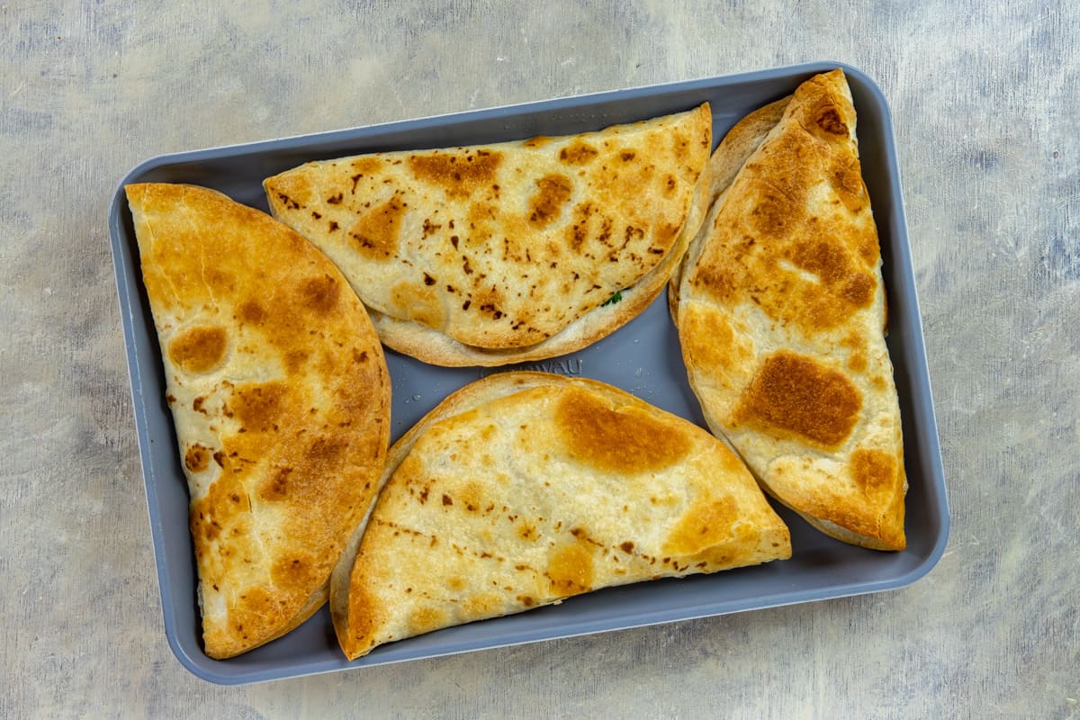 Four toasted and filled tortillas on sheet pan.