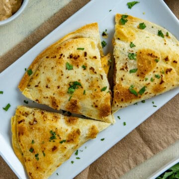 Three chicken quesadillas on white rectangular plate garnished with cilantro flakes.